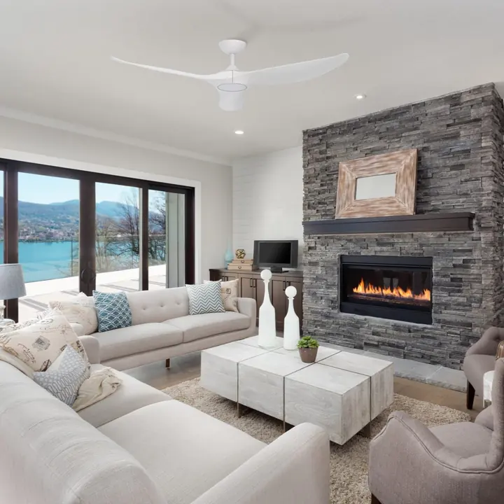 A white ceiling fan above a lounge room with a stone fireplace