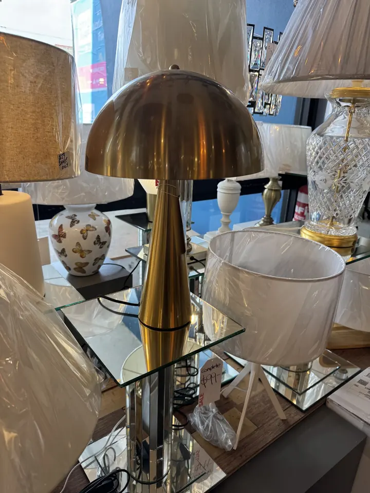 A brass mushroom table lamp lit among the lamps on the Cosmo Lighting showroom shelves