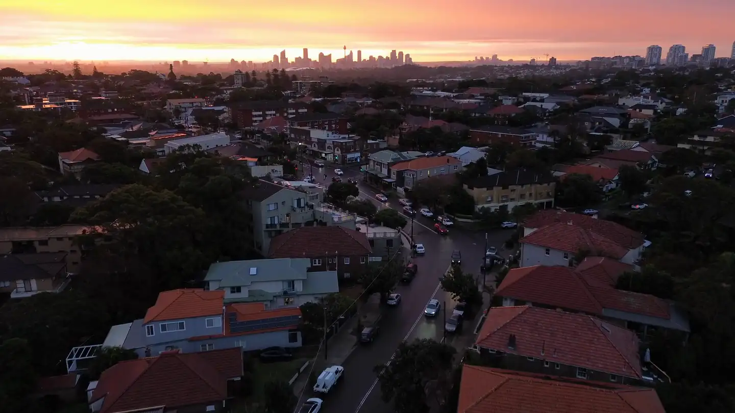 Drone view over Clovelly rooftops towards the Sydney skyline at sunset